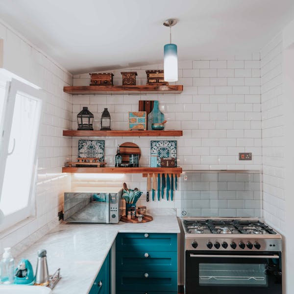 Bright modern kitchen with shelves, stove, and teal cabinets.