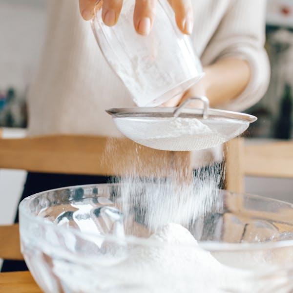 Close-up of hands sifting flour into a glass bowl, ideal for baking tutorials or food blogs.