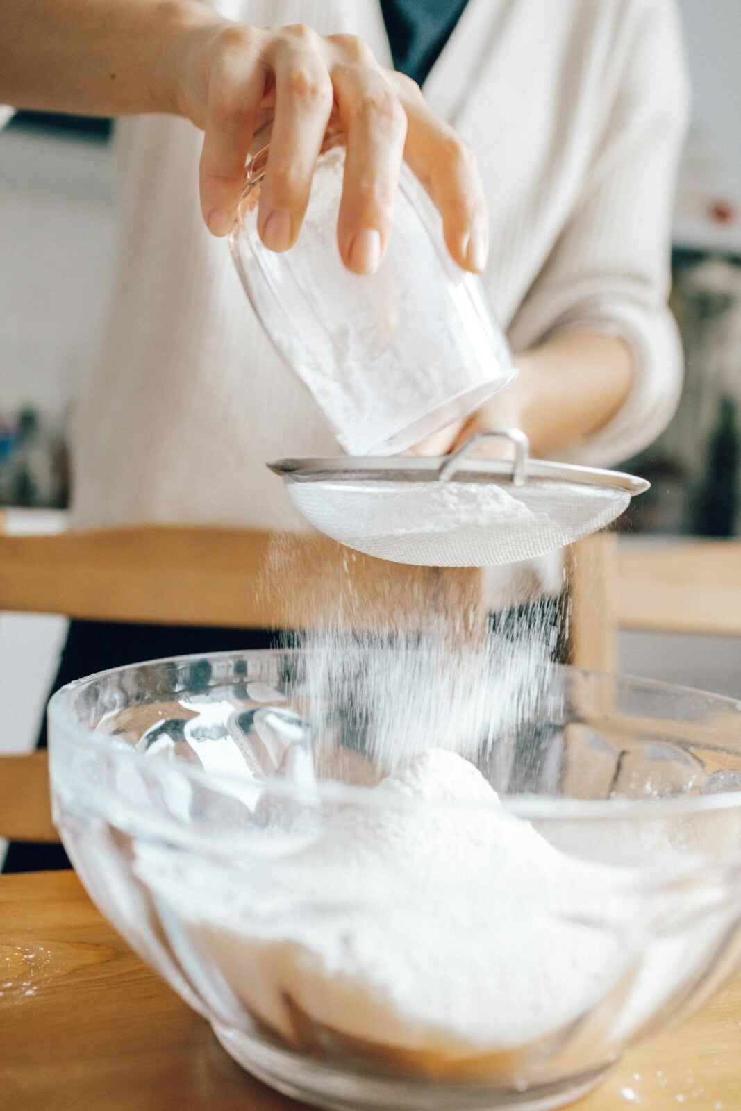 Close-up of hands sifting flour into a glass bowl, ideal for baking tutorials or food blogs.