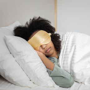 A woman peacefully sleeping with an eye mask in a cozy white bedroom setting.