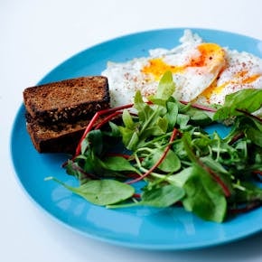 Delicious breakfast featuring fried eggs, toast, and fresh greens served on a vibrant blue plate.