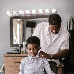 Barber prepares a young boy for a haircut in a cozy barbershop setting.