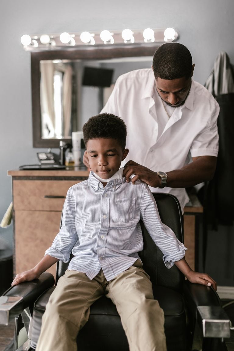 Barber prepares a young boy for a haircut in a cozy barbershop setting.