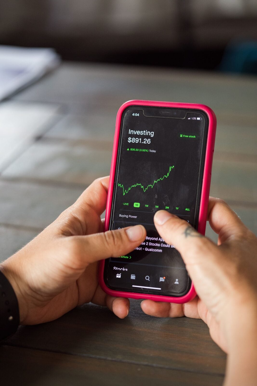 Close-up of hands holding a smartphone with stock market data on the screen.