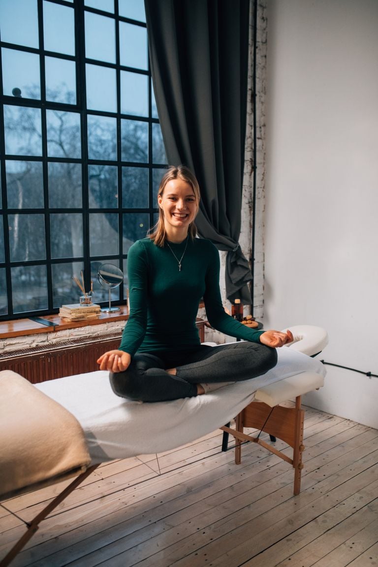 Woman in meditation pose on massage table, serene indoor setting, natural light.