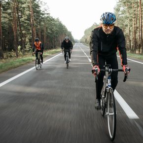 Group of cyclists riding through a forest on a quiet road during the day.