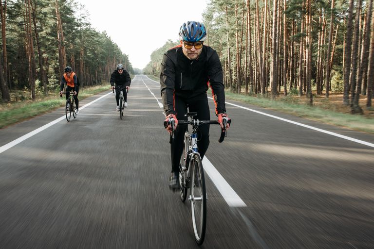 Group of cyclists riding through a forest on a quiet road during the day.