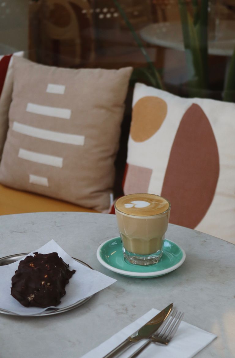 Inviting café scene featuring a latte and pastry on a marble table with decorative pillows.