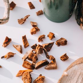 Top-down view of reishi mushroom pieces and a mug of hot drink on a wooden surface.