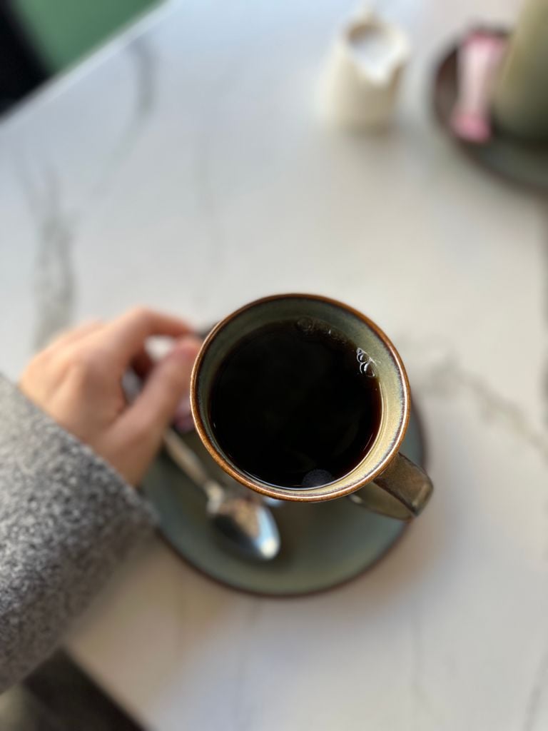 A hand holds a cup of coffee on a marble table, creating a cozy, warm ambiance.