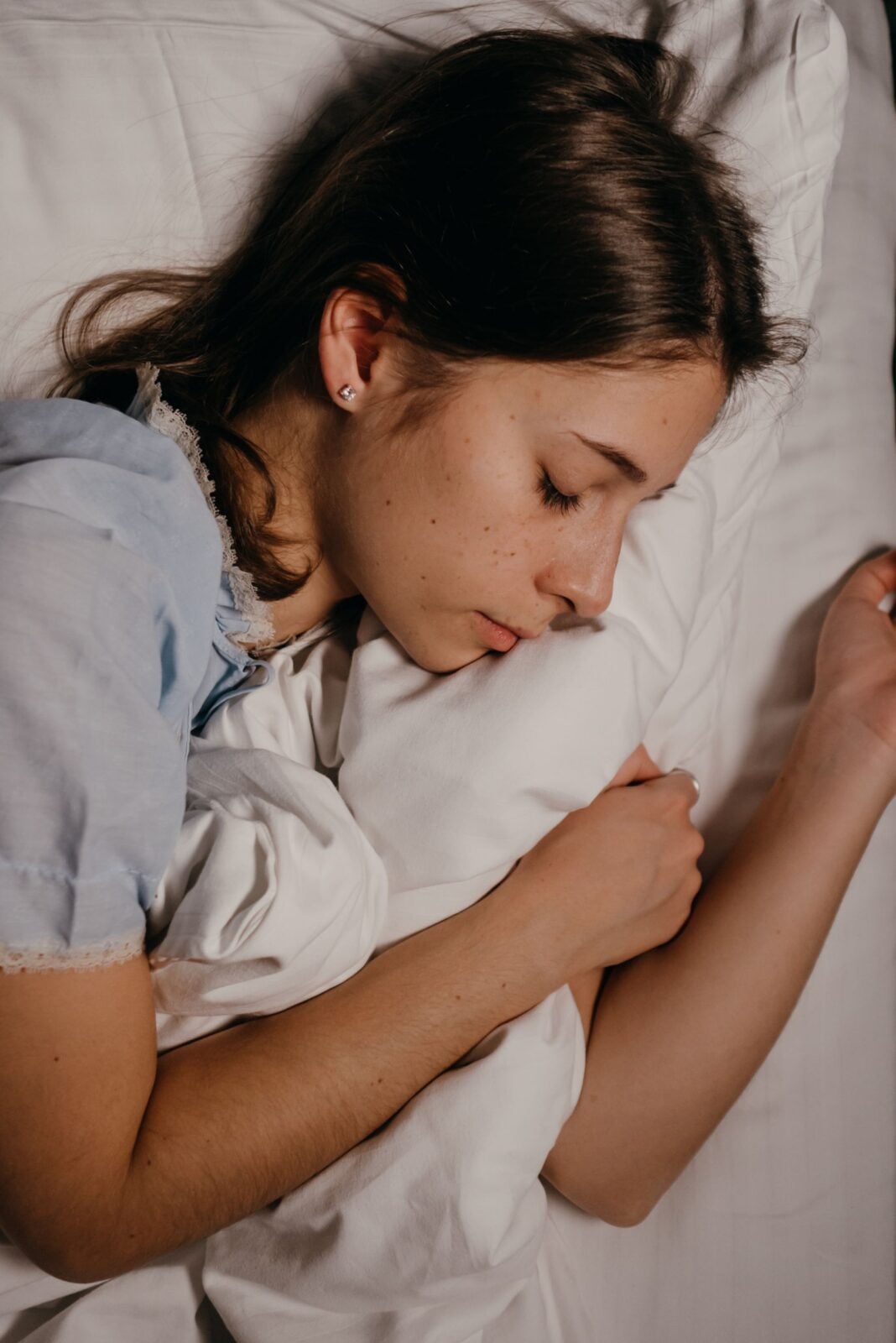 A young woman sleeping peacefully in bed, embracing a pillow, conveying relaxation and comfort.