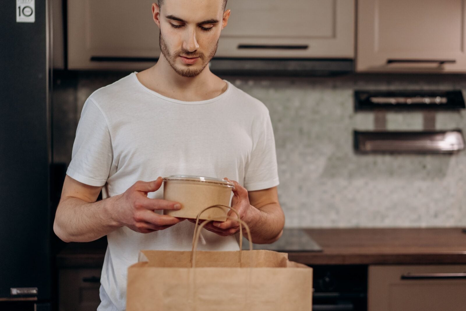 Adult man in a kitchen unpacking food delivery from a paper bag, showcasing eco-friendly packaging.