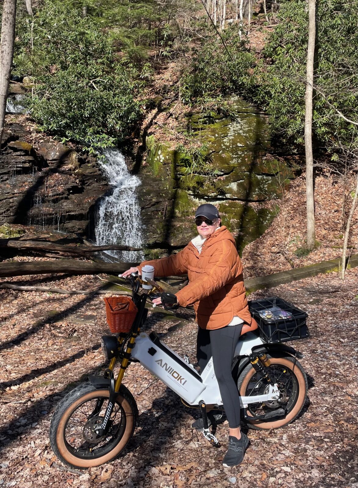 Hayley on Comet, her white ANIIOKI e-bike, beside a woodland waterfall.