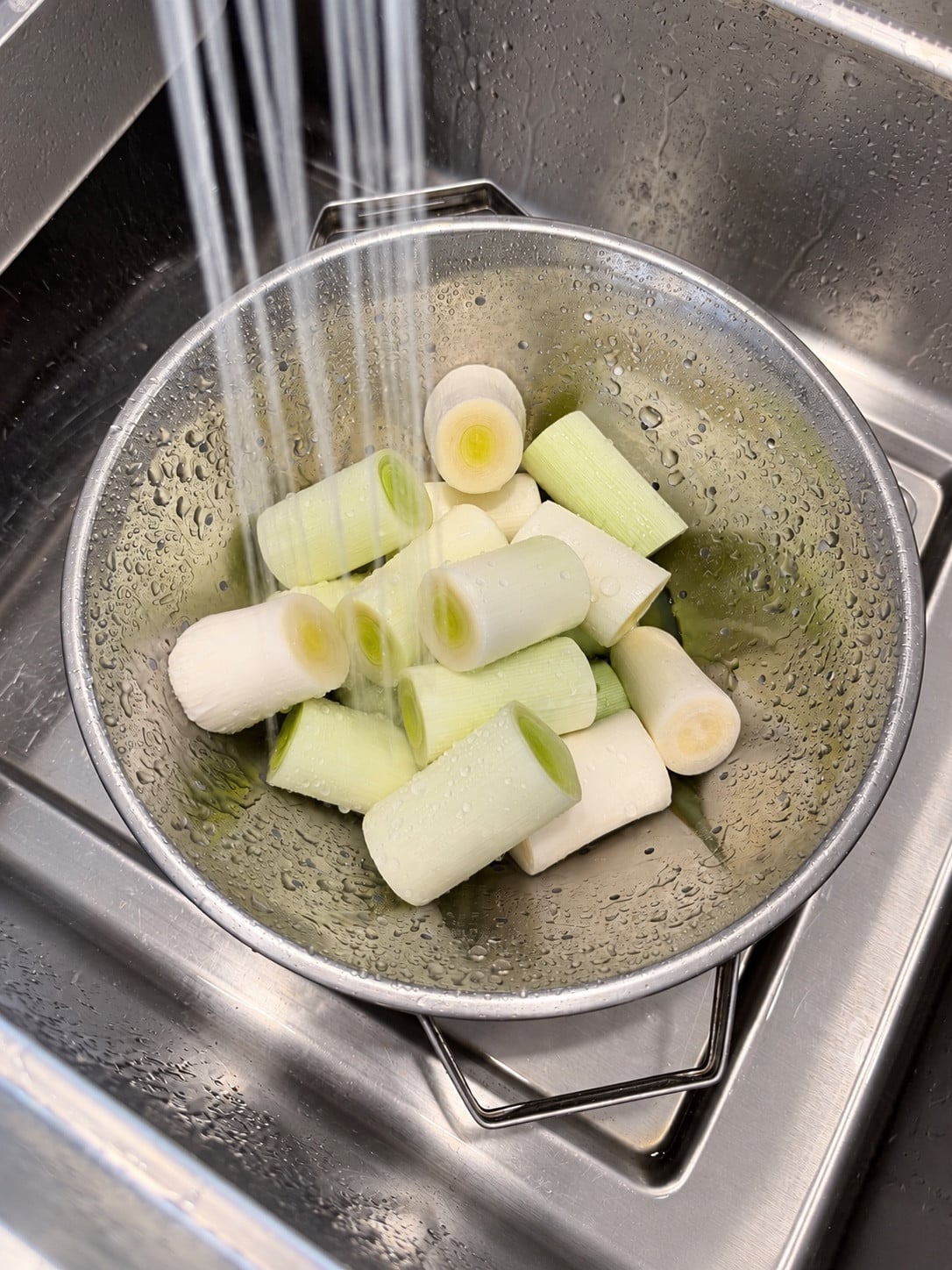 Leek rounds rinsing under running water in a colander