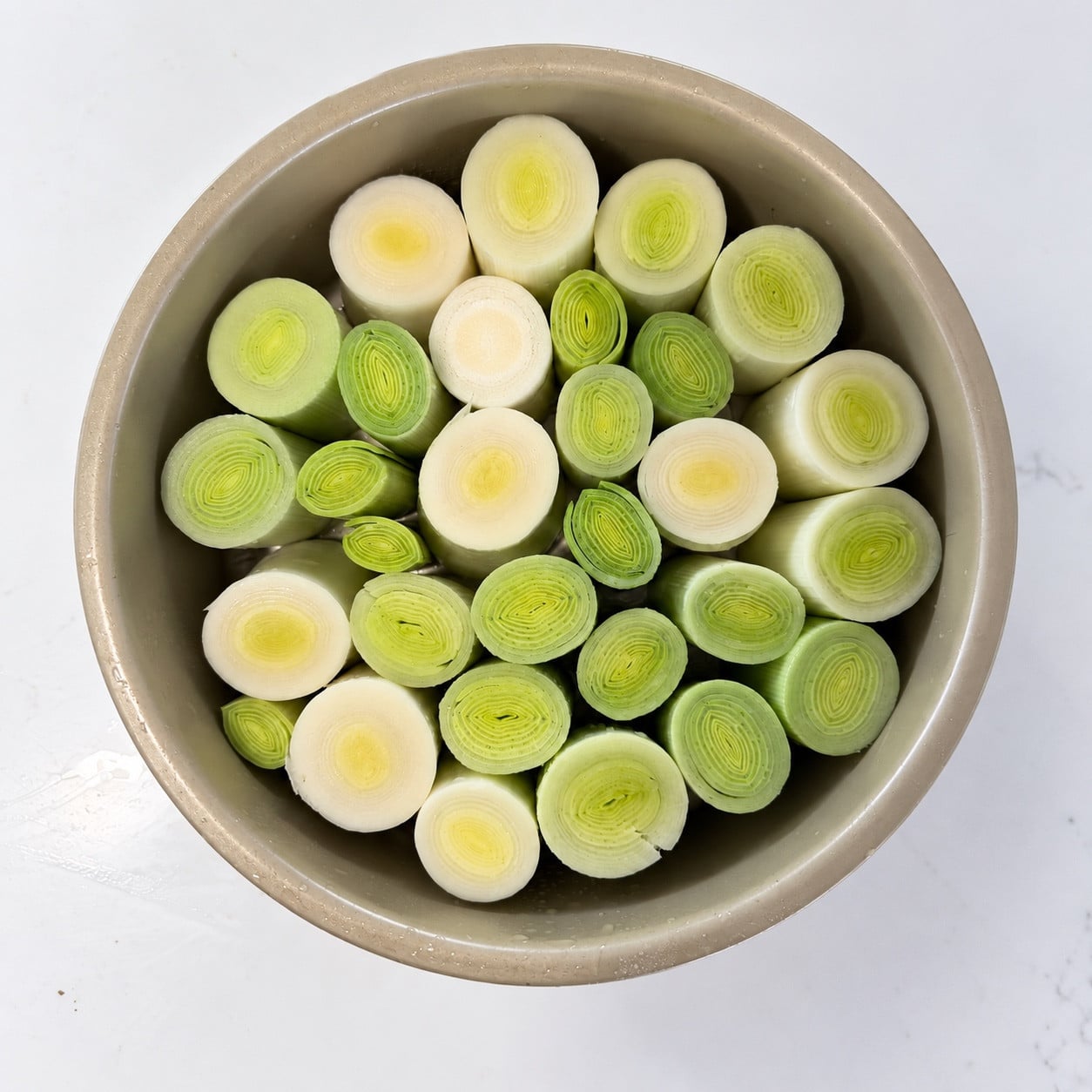 Raw leek rounds standing upright in a round baking pan
