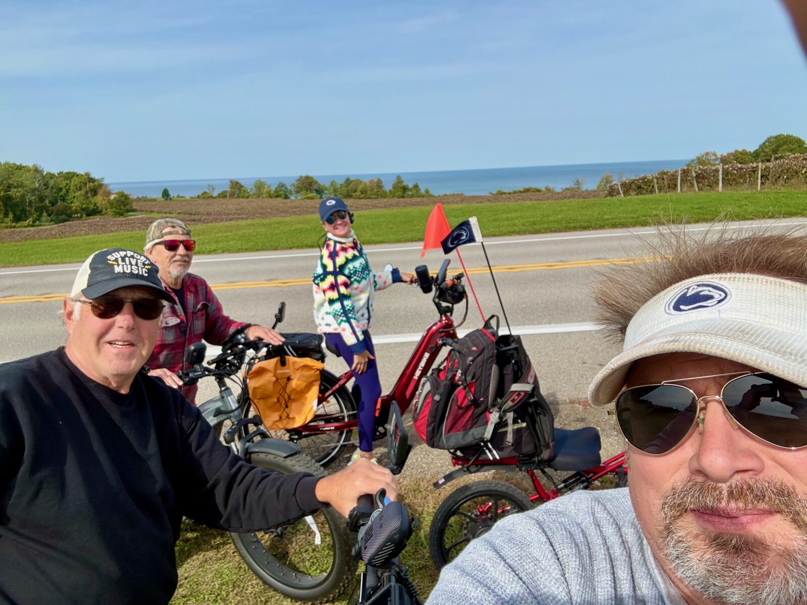 Hayley and friends paused with their e-bikes beside a lakeside road, including Ruby with orange panniers.