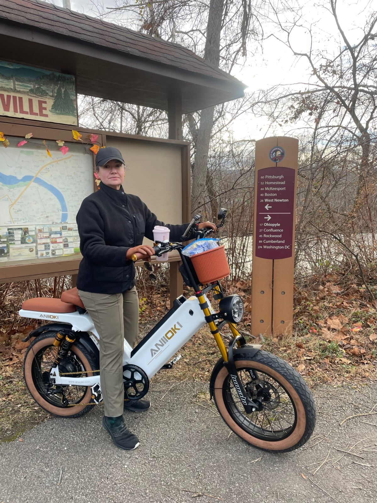 Hayley with Comet, her white ANIIOKI e-bike, beside a GAP trail sign