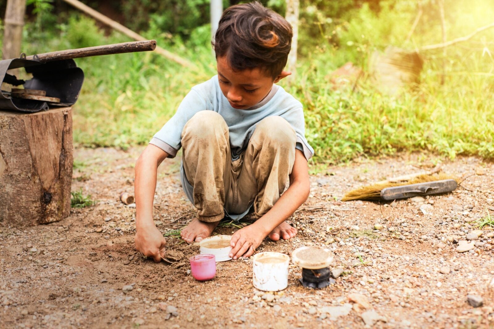 A young boy sitting on the ground playing with dirt and plastic cups in Indonesia.
