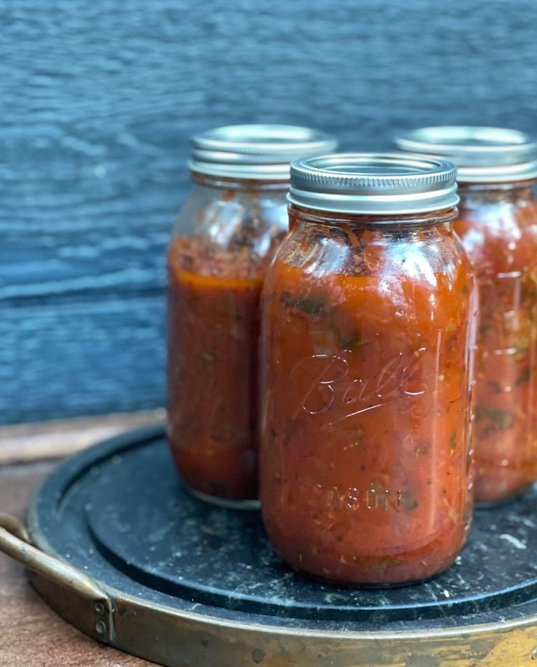 Close-up of homemade salsa in glass mason jars on a rustic tray, highlighting food preservation.