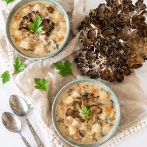 Two bowls of maitake mushroom chowder with potatoes and carrots beside a fresh maitake cluster