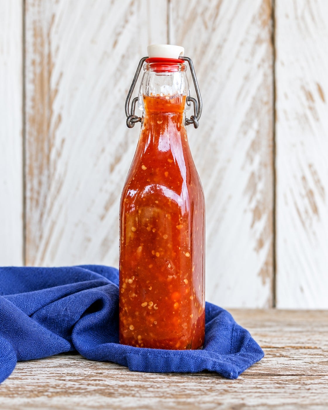 AI-enhanced illustration based on the original sweet chili sauce photograph, with a glass bottle on blue linen